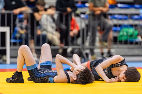 Two young wrestlers battle on a yellow mat, one pinning the other down during an intense youth match.