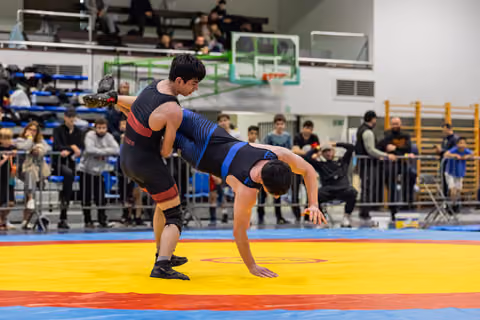 Young wrestler executes a powerful lift, hoisting his opponent off the colorful mat before a crowd of spectators indoors.