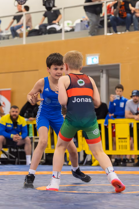 Two young boys face off on the mat, the boy in blue bracing confidently against Jonas in a dark singlet.