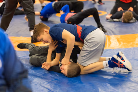 Determined boy in blue singlet pins opponent to the mat during a youth wrestling practice session.