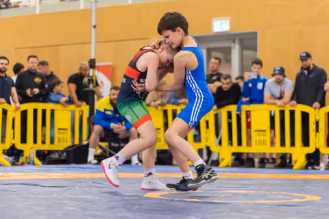 Two youth wrestlers locked in a tight clinch on the mat, both straining with effort during a competitive bout.
