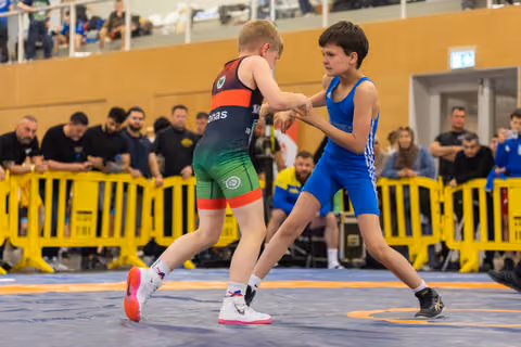 Two young boys face off on the wrestling mat, both in athletic stance, focused and determined during their bout.
