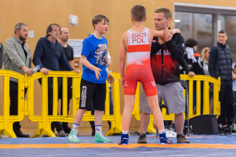 Coach places hand on shoulder of young Polish wrestler (Leonarczyk) while another boy watches on the mat.