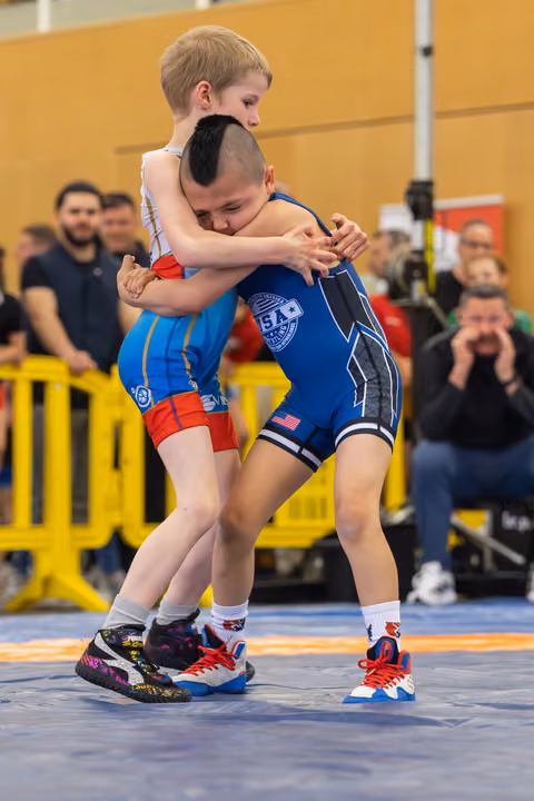 Two young wrestlers locked in a tight clinch on the mat, the boy in blue USA singlet driving forward with determination.