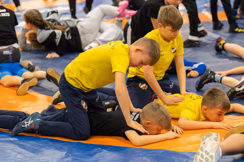 Boys in yellow jerseys practice wrestling holds on an orange mat, focused and engaged during a youth sports session.