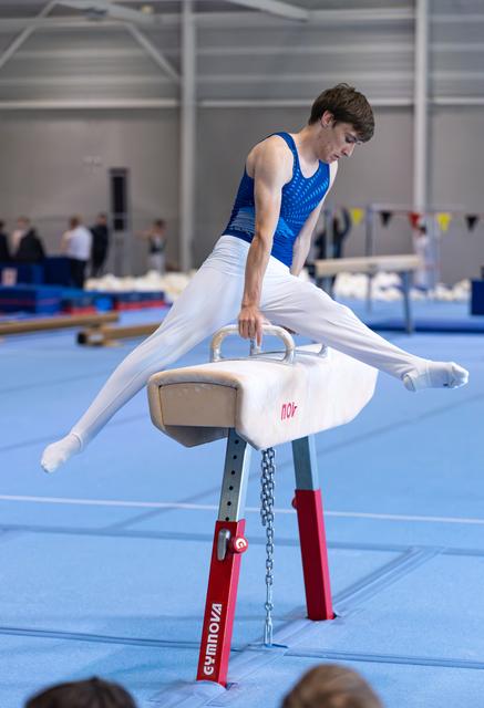 Young male gymnast performing a split position on pommel horse, demonstrating strength and control in training facility